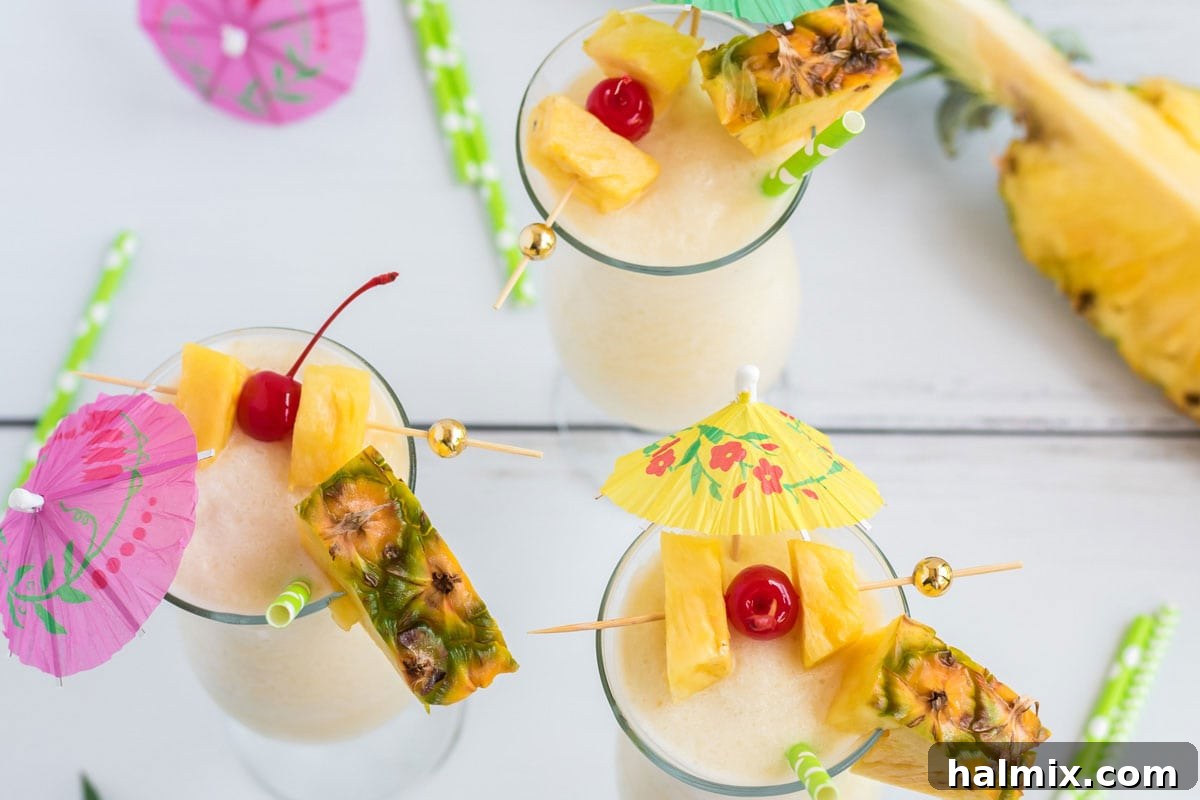 Three perfectly garnished Pina Coladas, adorned with pineapple wedges, maraschino cherries, and colorful cocktail umbrellas, ready for a party.