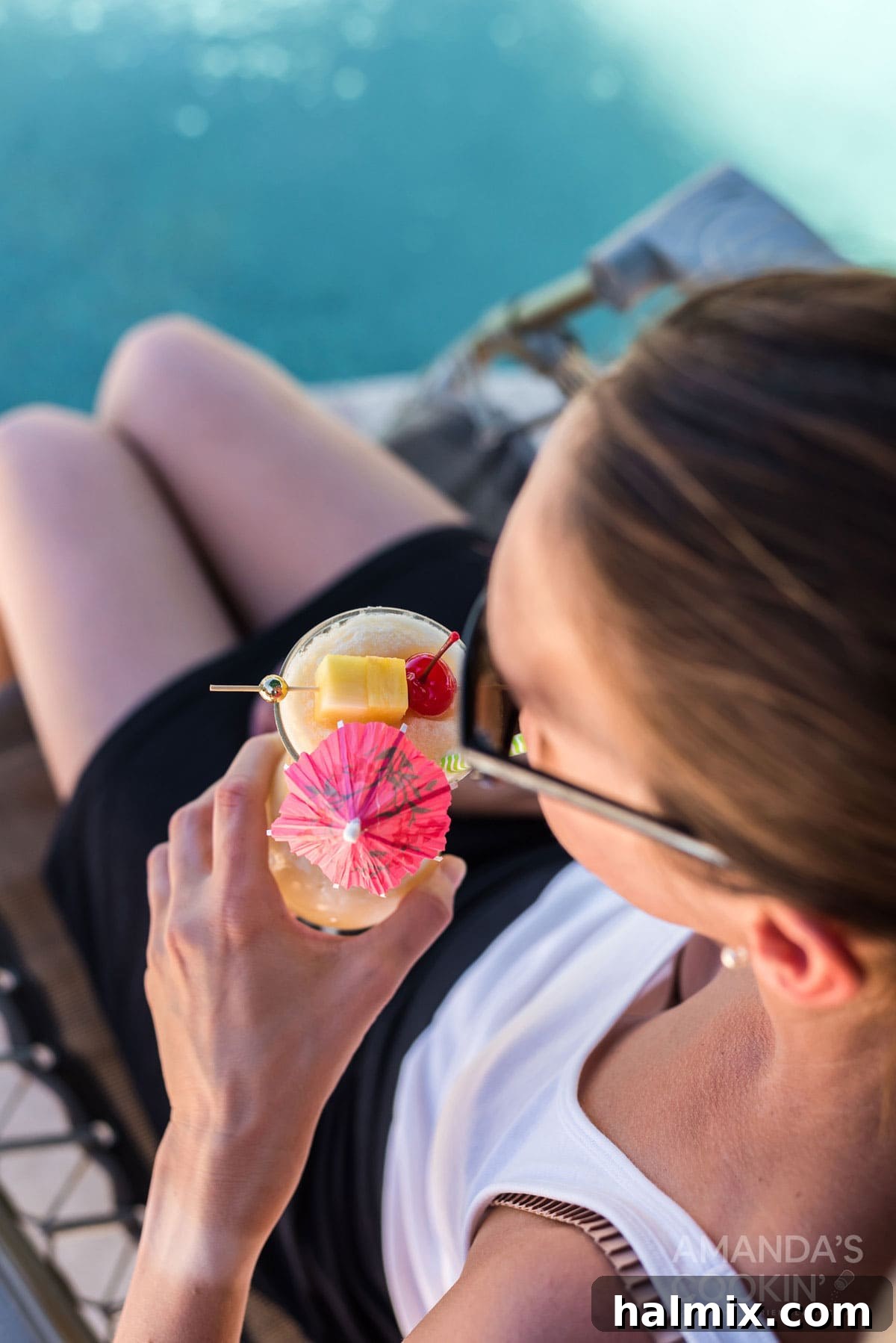 A woman enjoys a refreshing sip of her Pina Colada, looking relaxed and content, against a blurred background of a sunny outdoor setting.
