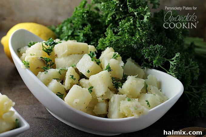 A close up of a long white bowl filled with Mediterranean potato salad and topped with chopped parsley.