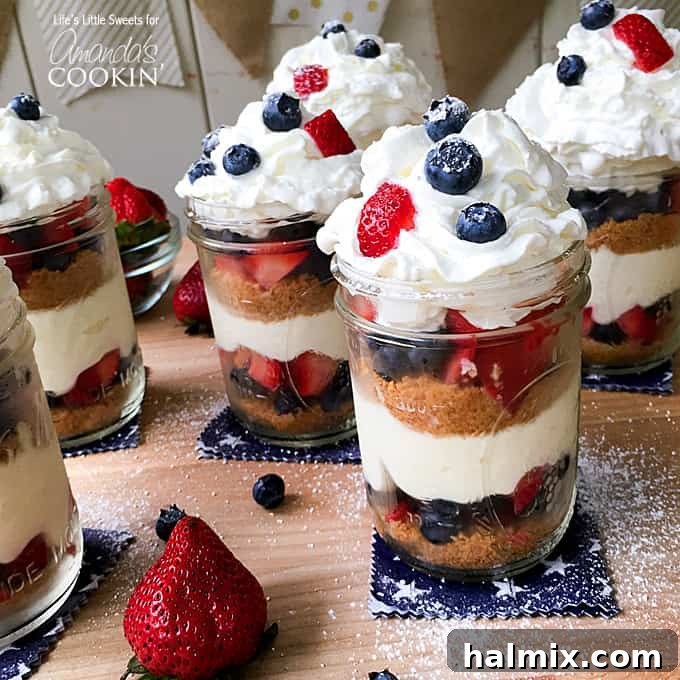 No-Bake Berry Cheesecake Trifle Jars 2 A close up of no bake berry cheesecake trifles in mason jars on a wooden cutting board.