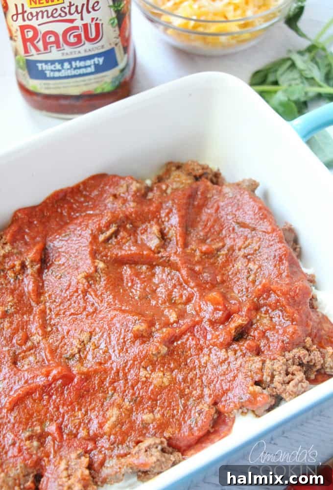 Layered Pizza Bake 11 An overhead photo of homestyle Ragu sauce being poured over layers of ground beef, pepperoni, ricotta, and noodles in a dish.