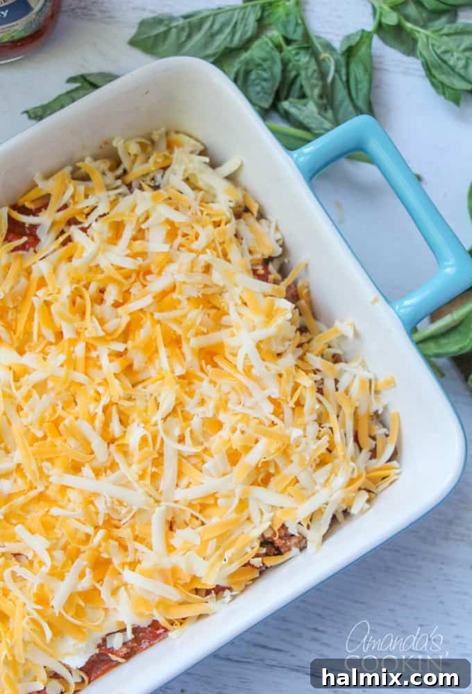 Layered Pizza Bake 12 An overhead photo of shredded cheddar cheese layered over Ragu sauce, ground beef, pepperoni, ricotta, and noodles.