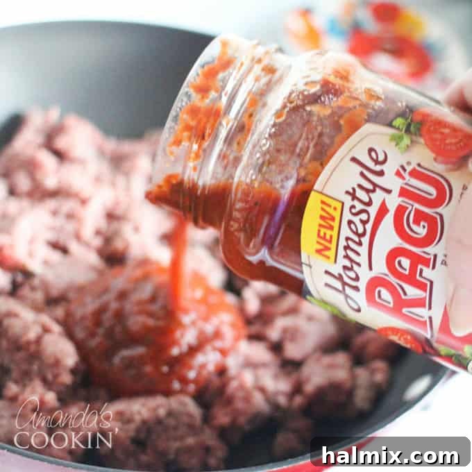 Layered Pizza Bake 6 A close up photo of Ragu sauce being poured into a skillet of browned ground beef.