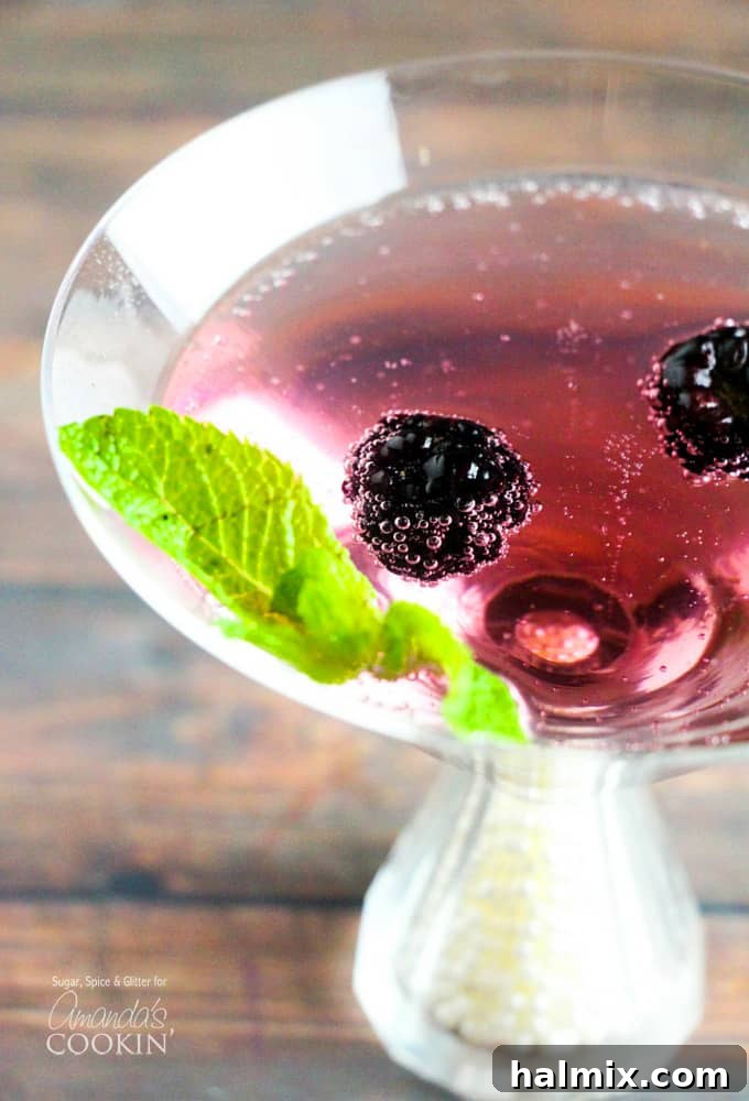 A close up overhead of a blackberry gin martini topped with fresh blackberries and mint leaves.