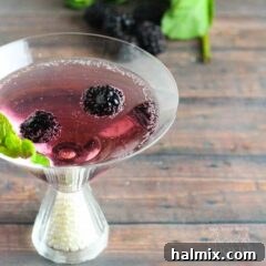 A close up of a blackberry gin martini topped with fresh blackberries and mint leaves.