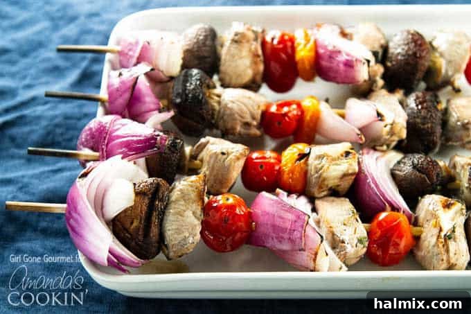 Succulent Grilled Chicken Skewers 5 A close up of marinated chicken skewers with tomatoes, red onions and mushrooms.