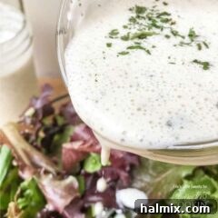A close up photo of buttermilk ranch dressing being poured over a salad.