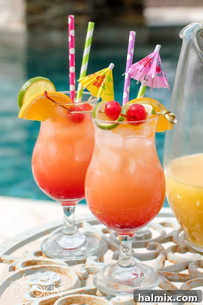 Island Elixir 2 Two glasses of vibrant rum punch and a pitcher, perfectly set by a sparkling blue swimming pool, garnished with fresh fruit slices, inviting a refreshing sip.