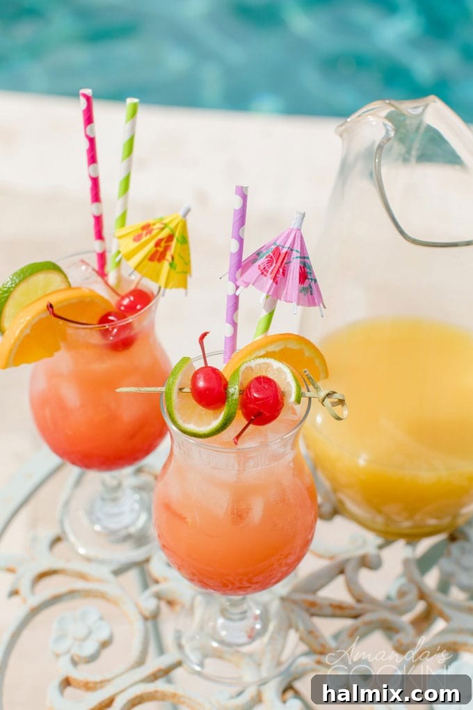 Island Elixir 3 Two enticing glasses of Caribbean rum punch garnished with orange and lime slices, alongside a full pitcher, all shimmering by a sunlit pool, ready for summer enjoyment.