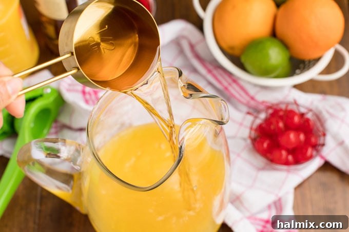 Island Elixir 6 A hand pouring golden rum into a large pitcher filled with a vibrant mix of orange and pineapple juices, illustrating a key step in making rum punch.