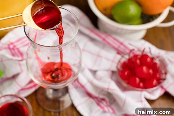 Island Elixir 7 A clear hurricane glass receiving a pour of grenadine syrup at the bottom, creating a vibrant red layer before the rum punch is added.