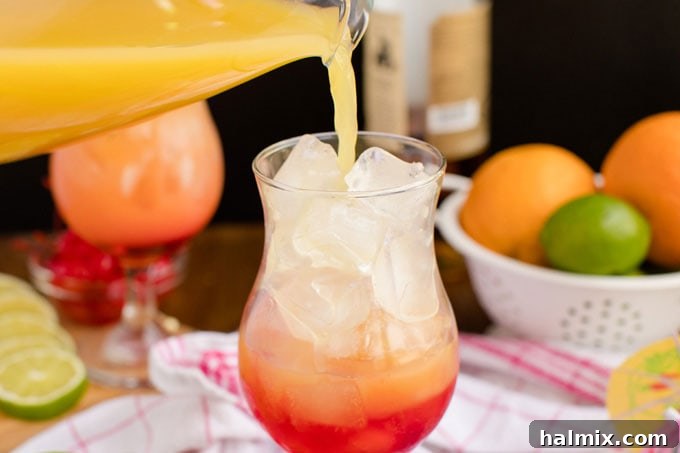 Island Elixir 9 A refreshing rum punch being carefully poured into a glass filled with ice and grenadine, creating a beautiful sunset-like gradient of red to orange.