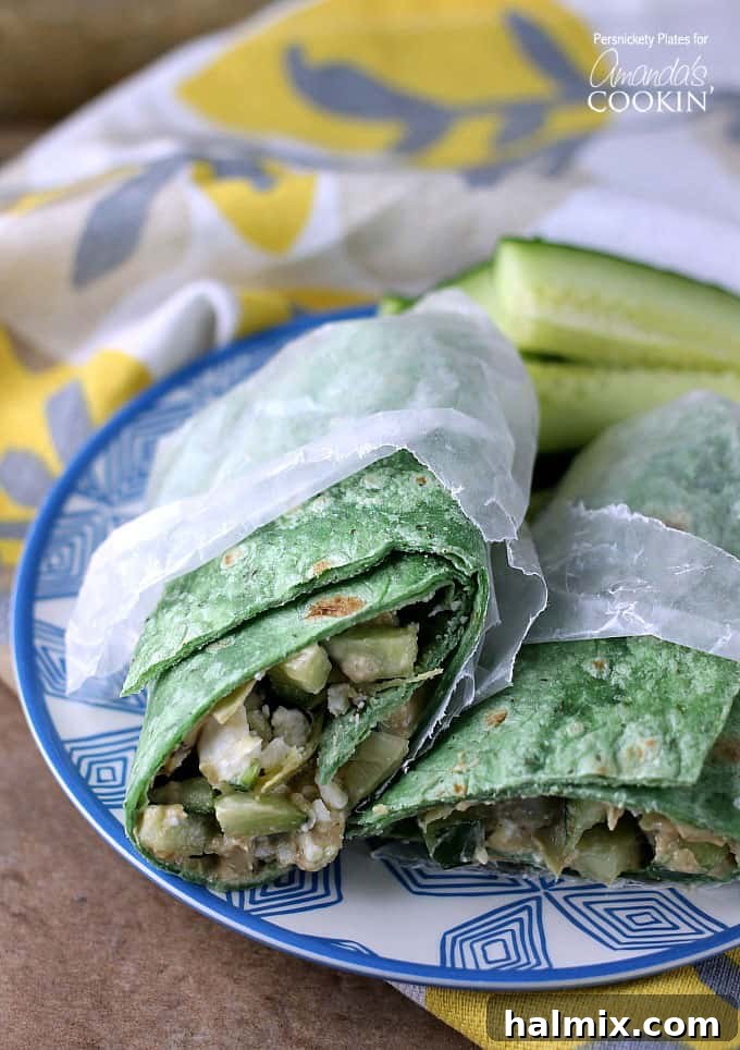 Two halves of a vibrant Mediterranean veggie wrap, carefully wrapped in wax paper, resting side-by-side on an elegant blue and white patterned plate, showcasing its fresh, healthy appeal.