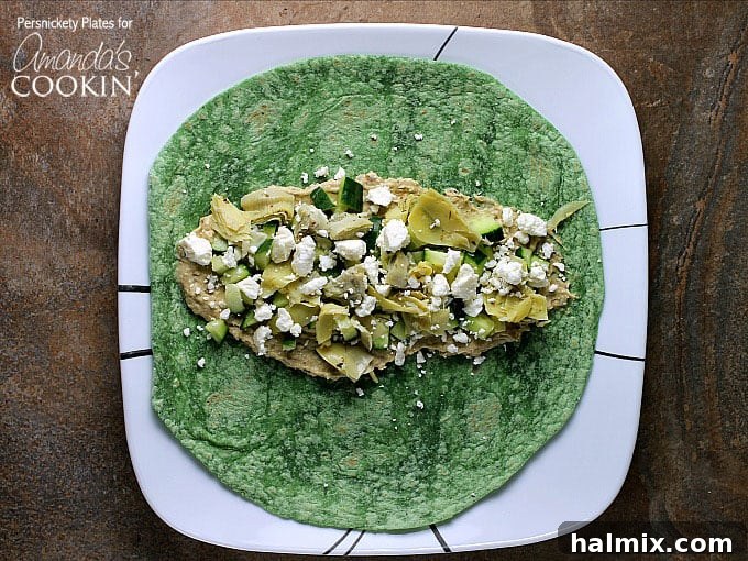 An inviting overhead photograph displaying the fresh, vibrant components of a Mediterranean veggie wrap: neatly chopped artichoke hearts, finely diced cucumber, a generous swirl of creamy hummus, and crumbled feta cheese, all artfully arranged on a spinach wrap.
