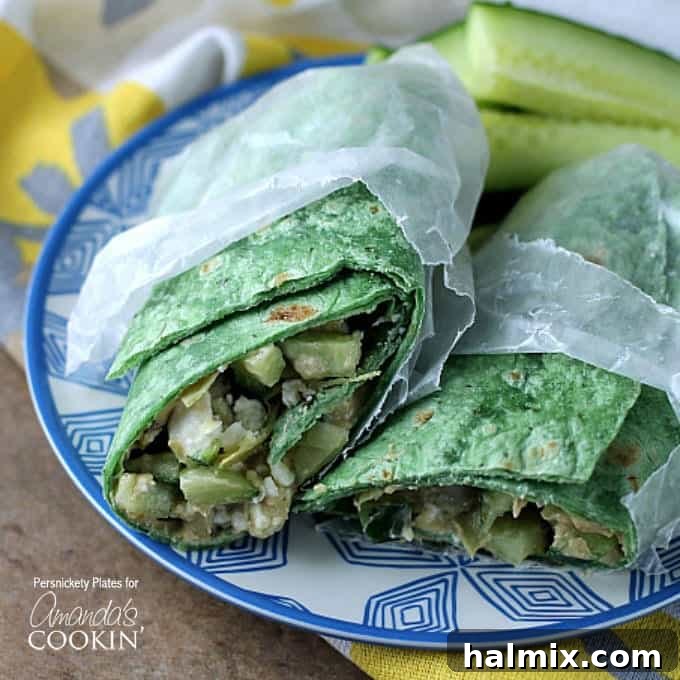 Close-up of two perfectly rolled and halved Mediterranean veggie wraps, presented in wax paper on a decorative blue and white plate, highlighting their appetizing layers and readiness to be enjoyed.