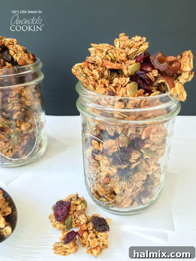 A close up photo of autumn harvest fruit and nut granola in a clear mason jar, showcasing its layers and rich texture.