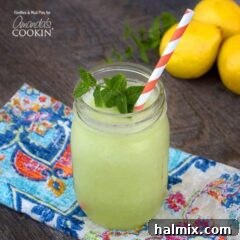 A mason jar filled with honeydew lemon slush topped with fresh mint and served with a red and white striped straw.