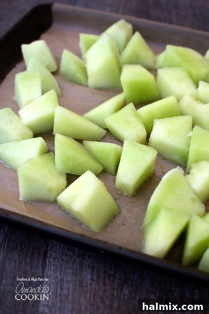 A close-up photo of freshly chopped honeydew melon cubes, ready for freezing.