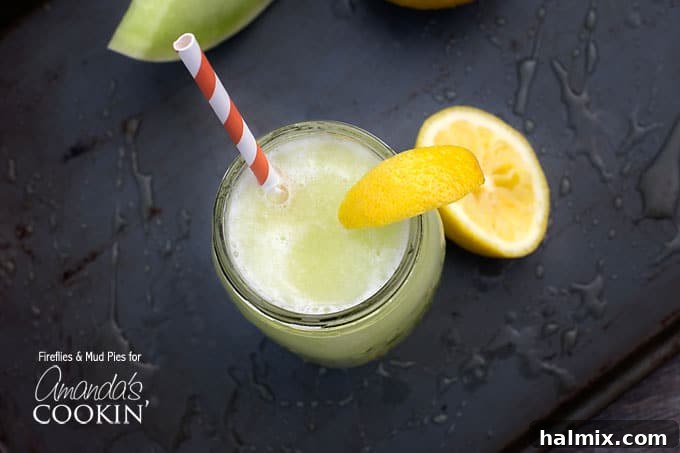 An overhead view of a mason jar filled with a bright green honeydew lemon slush, garnished with a lemon wedge and a red and white striped straw.