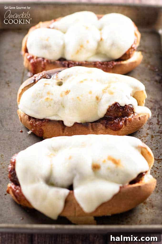 Saucy Slow Cooker BBQ Meatball Heroes 3 A close up photo of three slow cooker BBQ meatball subs topped with provolone cheese, showcasing the vibrant sauce and tender meatballs.