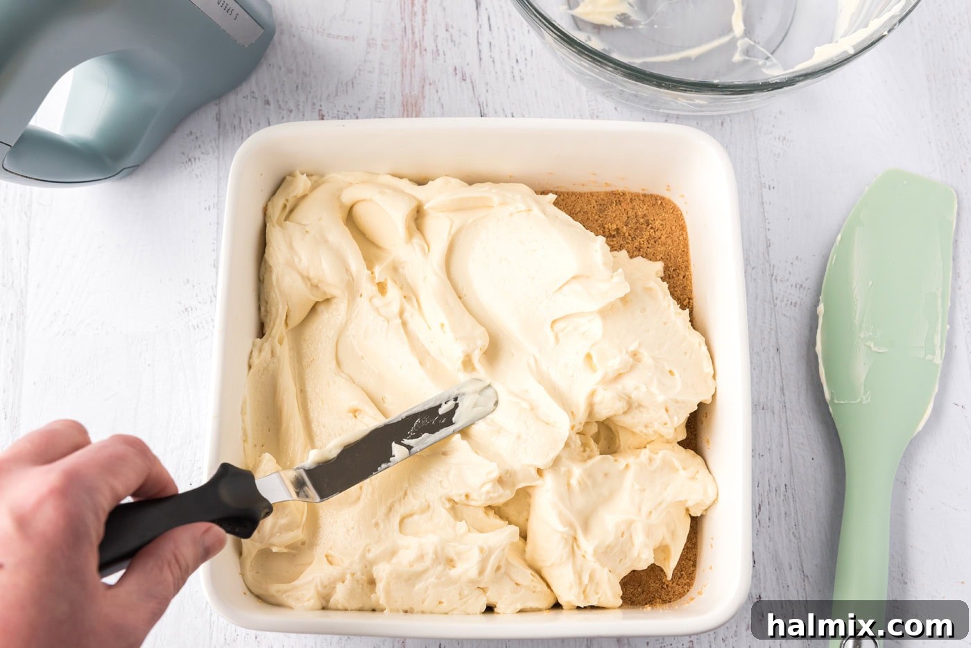 spreading mascarpone cheesecake over graham cracker crust in a pan