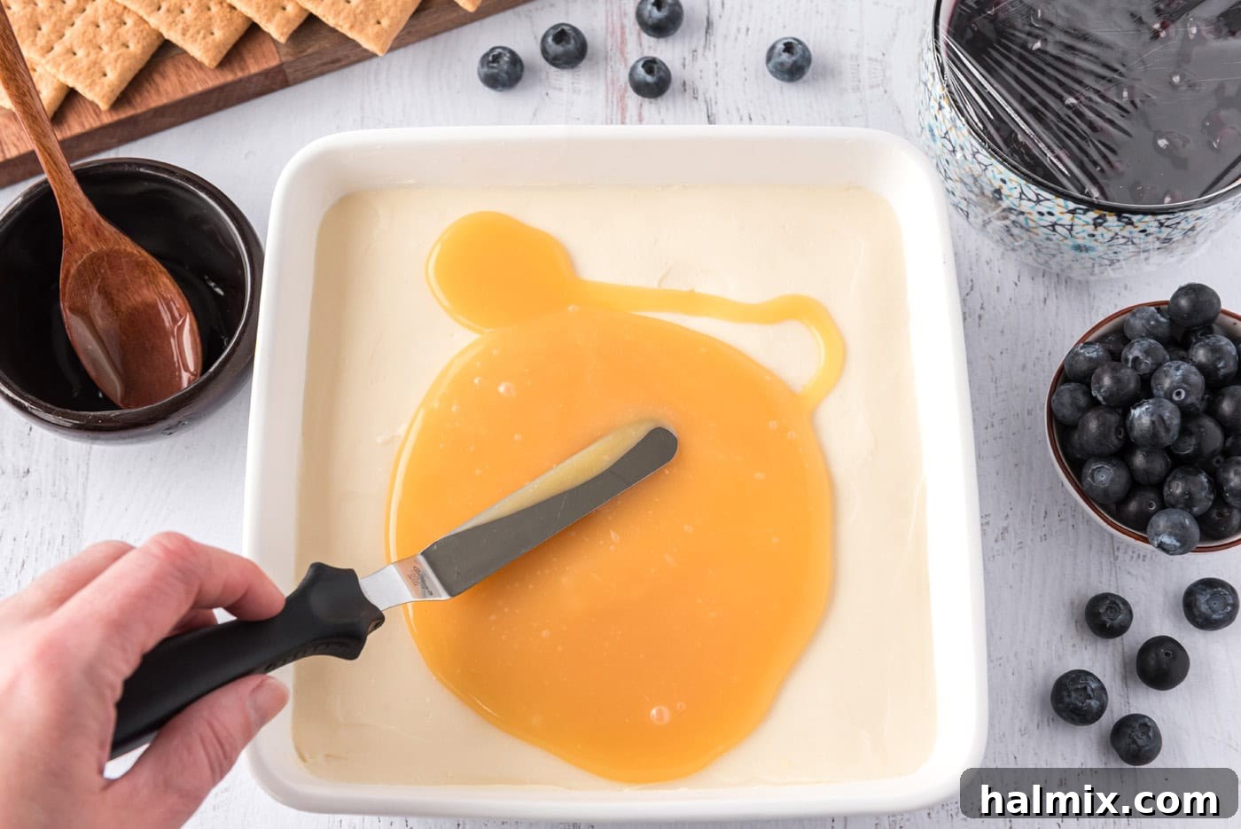 spreading lemon curd over chilled cheesecake in a square pan