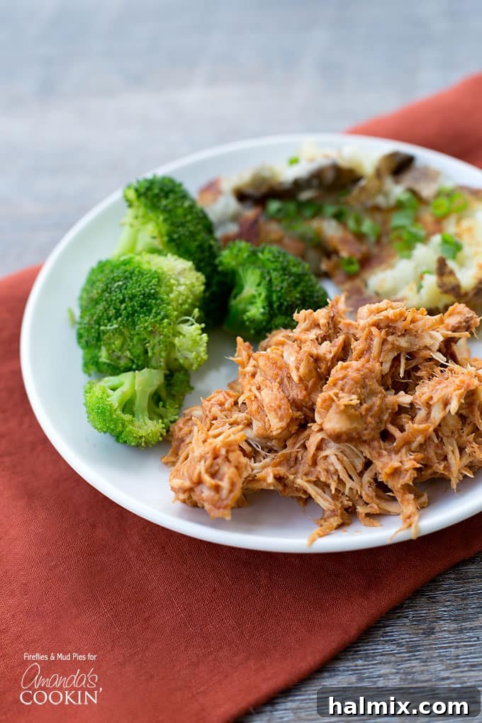 A close up photo of a plate of tender, shredded BBQ crockpot chicken served alongside vibrant steamed broccoli.