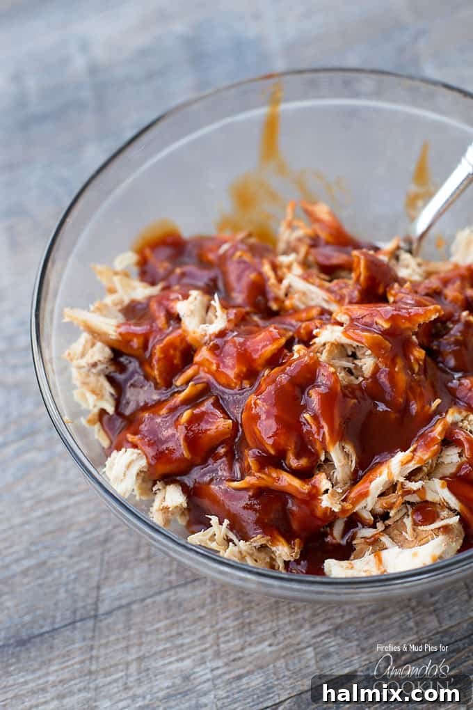 A clear glass bowl showcasing a generous portion of perfectly shredded chicken generously coated in a rich, glistening BBQ sauce.