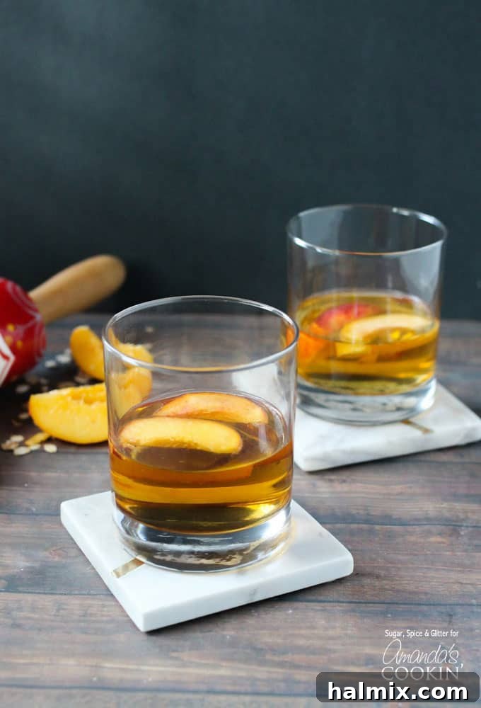 Two short clear glasses filled with peach pie cocktail with two peach slices floating on top.