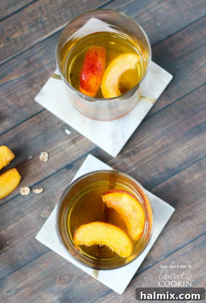 An overhead of two short clear glasses filled with peach pie cocktail with two peach slices floating on top.
