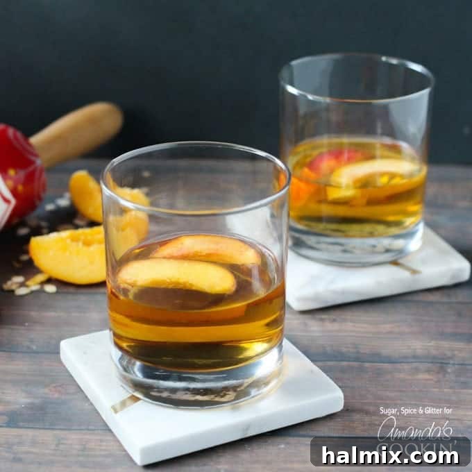 Two short clear glasses filled with peach pie cocktail with two peach slices floating on top.