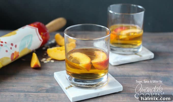 Two short clear glasses filled with peach pie cocktail with two peach slices floating on top.