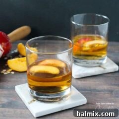 Two short clear glasses filled with peach pie cocktail with two peach slices floating on top.