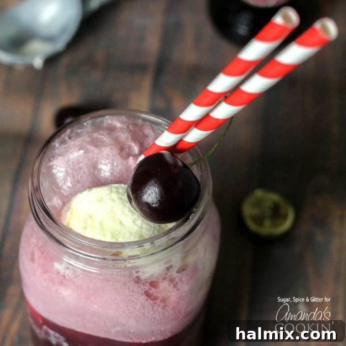 Velvet Cherry Float 3 A close-up view of the Black Cherry Float Cocktail in a mason jar, showcasing its frothy texture and vibrant color, with a single cherry garnish and striped straws.
