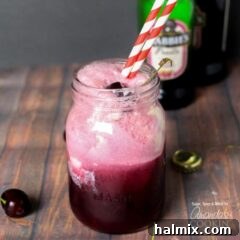A glass of a Black Cherry Float Cocktail on a table, garnished with a cherry.