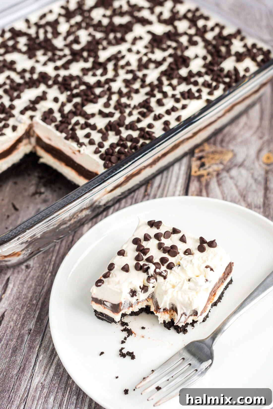 Slice of Chocolate Lasagna on a plate with a pan of Chocolate Lasagna behind it