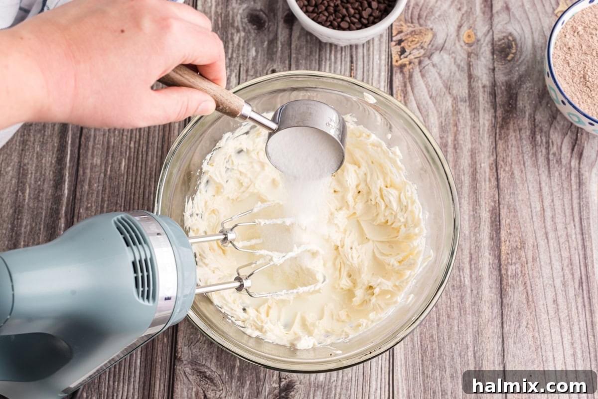 Sugar being added to a bowl of beaten cream cheese and milk