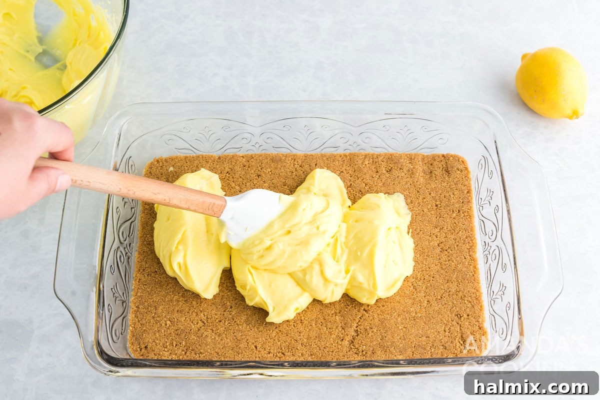 Spreading the lemon cream cheese pudding mixture evenly over the graham cracker crust in the pan.