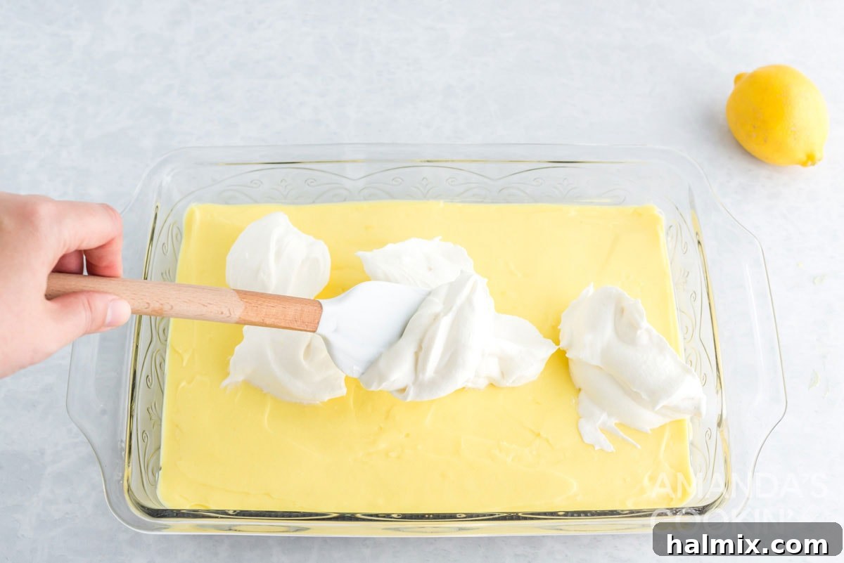 Spreading a layer of whipped topping over the lemon cream cheese mixture in the pan.