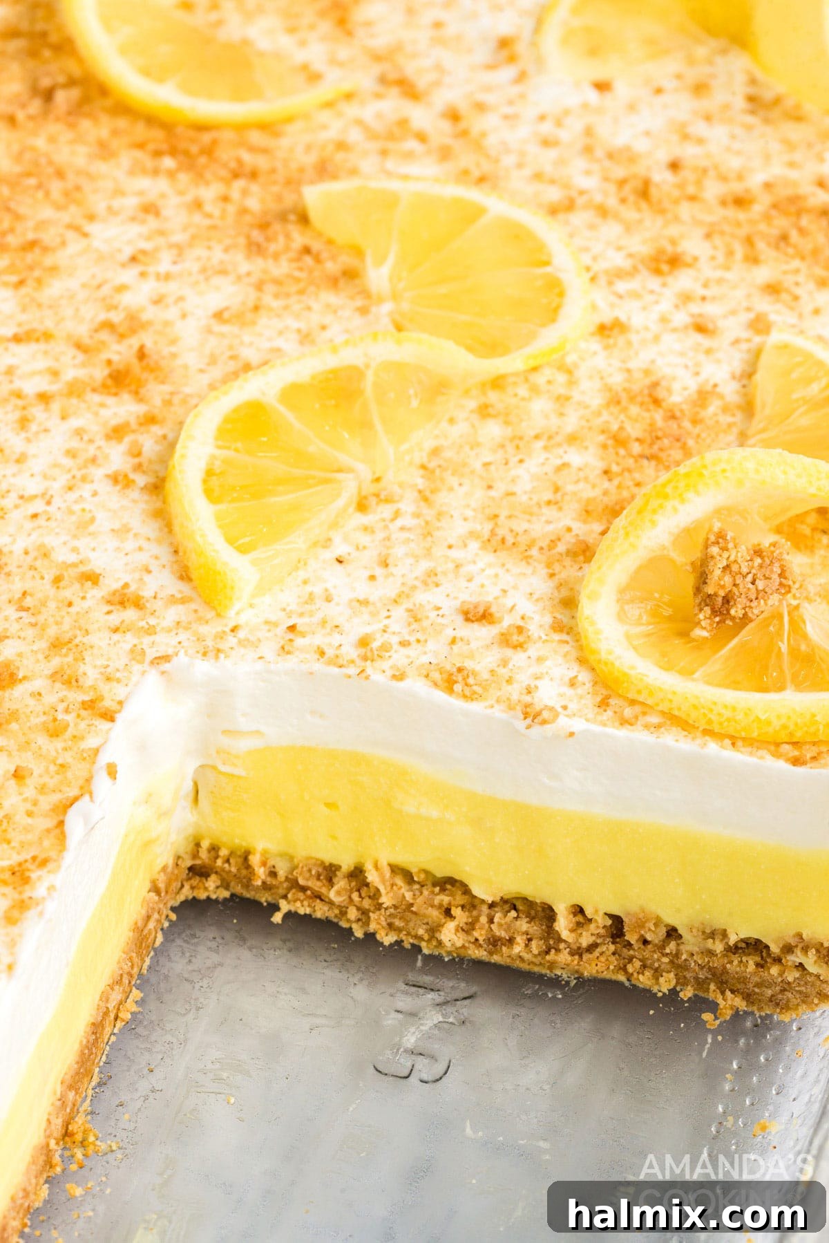 A layered lemon dessert in a 13x9 inch pan with one slice removed, showcasing the distinct layers of crust, creamy filling, and whipped topping.