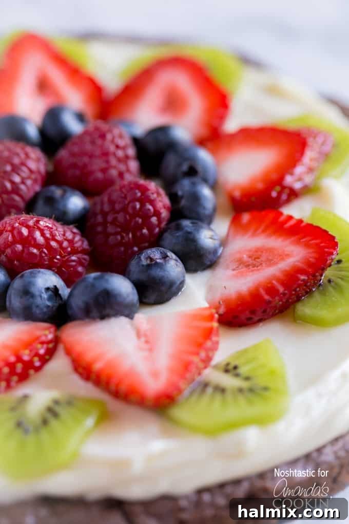 A close up of cut up strawberries, kiwi, blueberries and raspberries on a brownie pizza, showcasing its vibrant colors and delicious toppings.