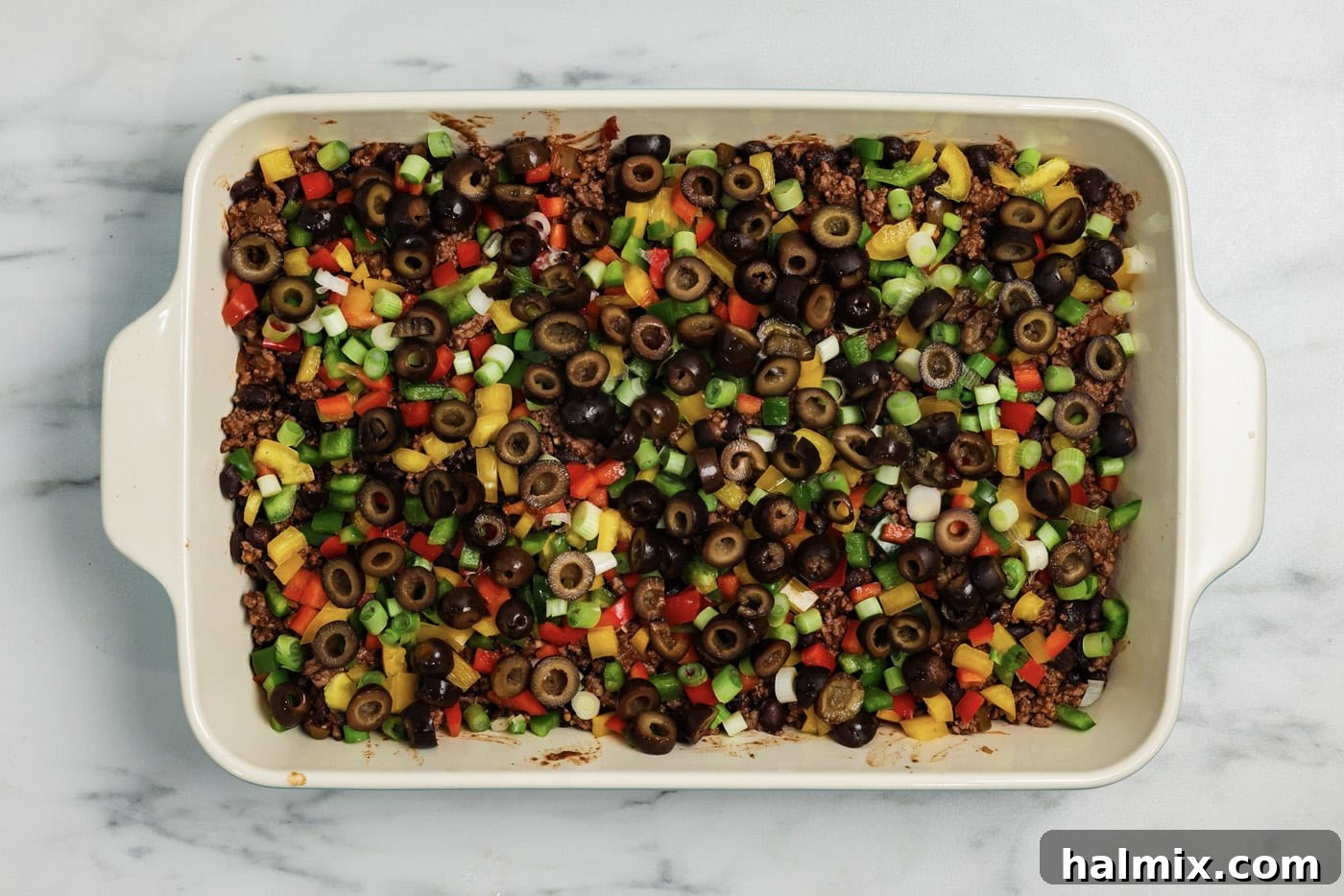 Ultimate Taco Bake 8 Black olives on top of ground beef mixture and fresh chopped vegetables