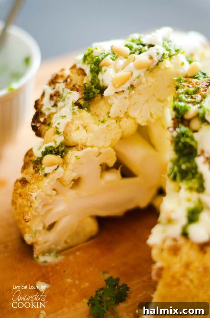 A close up of the center of a whole roasted cauliflower topped with whipped feta and herb sauce on a wooden cutting board.