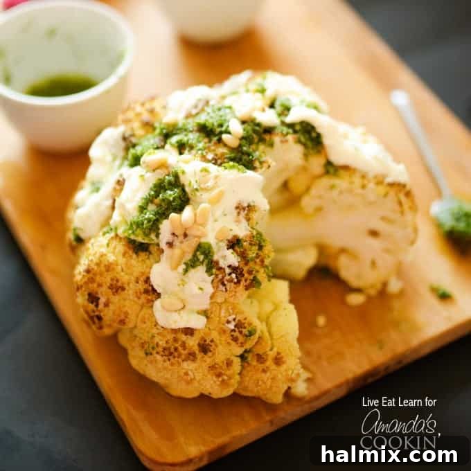 A close up of a whole roasted cauliflower topped with whipped feta and herb sauce on a wooden cutting board.