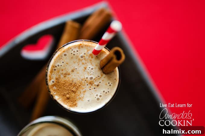 Creamy Cinnamon Swirl Delight 4 An overhead view of a tall clear glass filled with a cinnamon bun smoothie, adorned with a cinnamon stick and a red striped straw, beautifully composed.