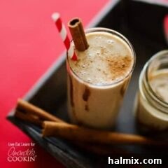 Creamy Cinnamon Swirl Delight 7 A tall clear glass filled with a cinnamon bun smoothie, served with a cinnamon stick and a red striped straw, highlighting its creamy texture.