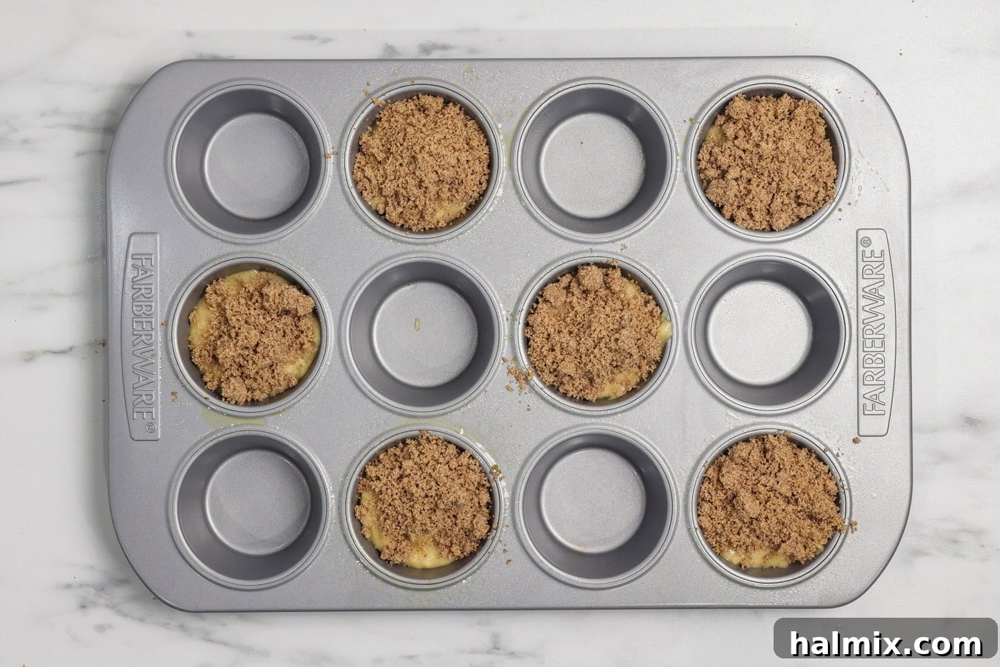 Cinnamon streusel added on top of vanilla muffin batter in a muffin pan