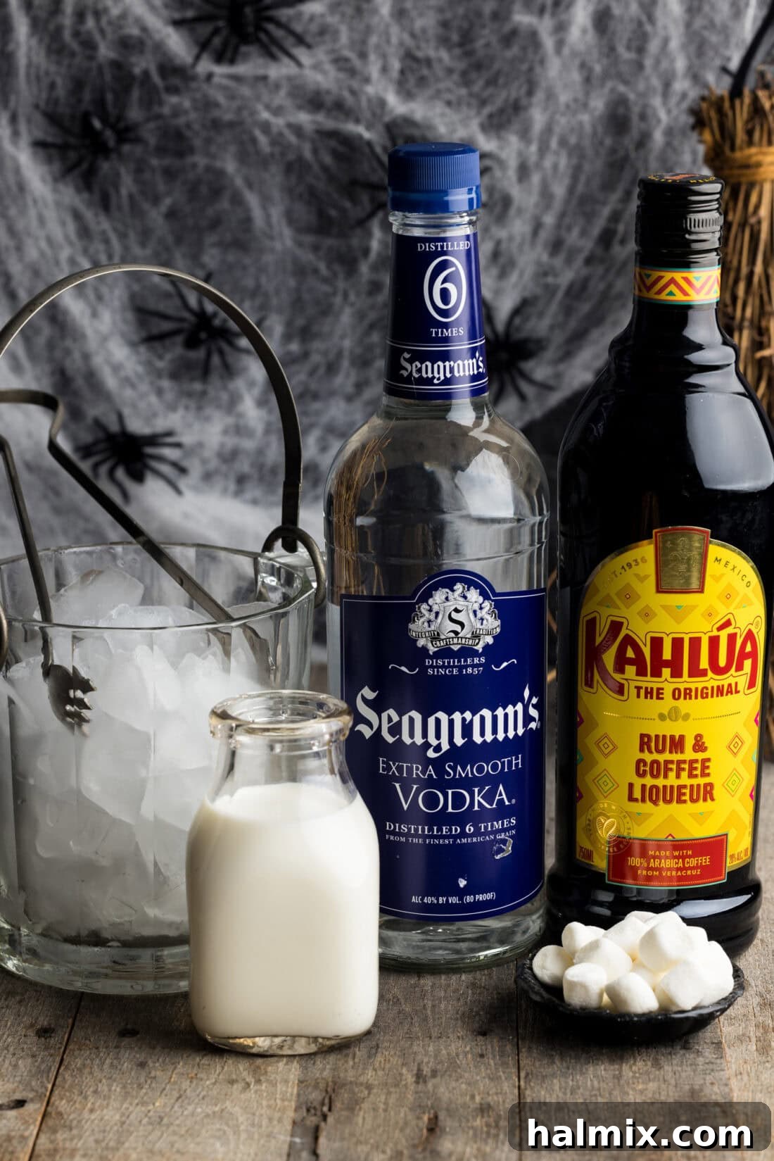 A flat lay photograph of all the ingredients needed for the Spiderweb Cocktail: Kahlua, vodka, heavy cream, and mini marshmallows, arranged neatly on a surface.