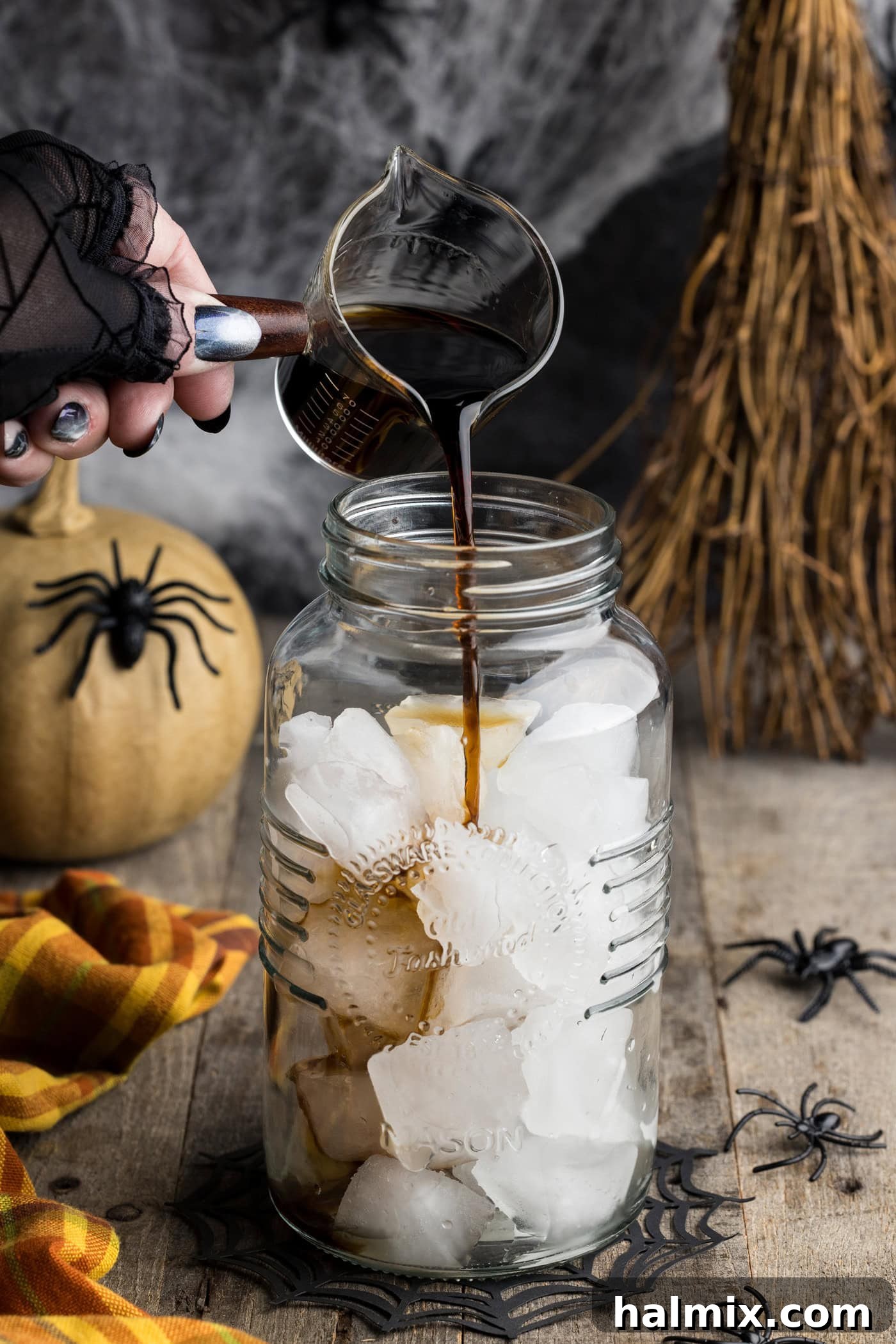 Pouring Kahlua coffee liqueur into a cocktail shaker filled with ice, illustrating the first step of mixing the Spiderweb Cocktail.