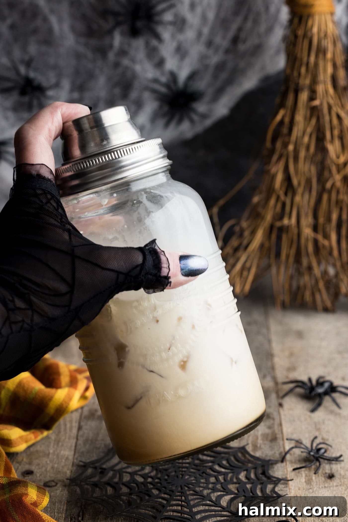 A hand holding a cocktail shaker vigorously, demonstrating the mixing process for the creamy Spiderweb Cocktail.